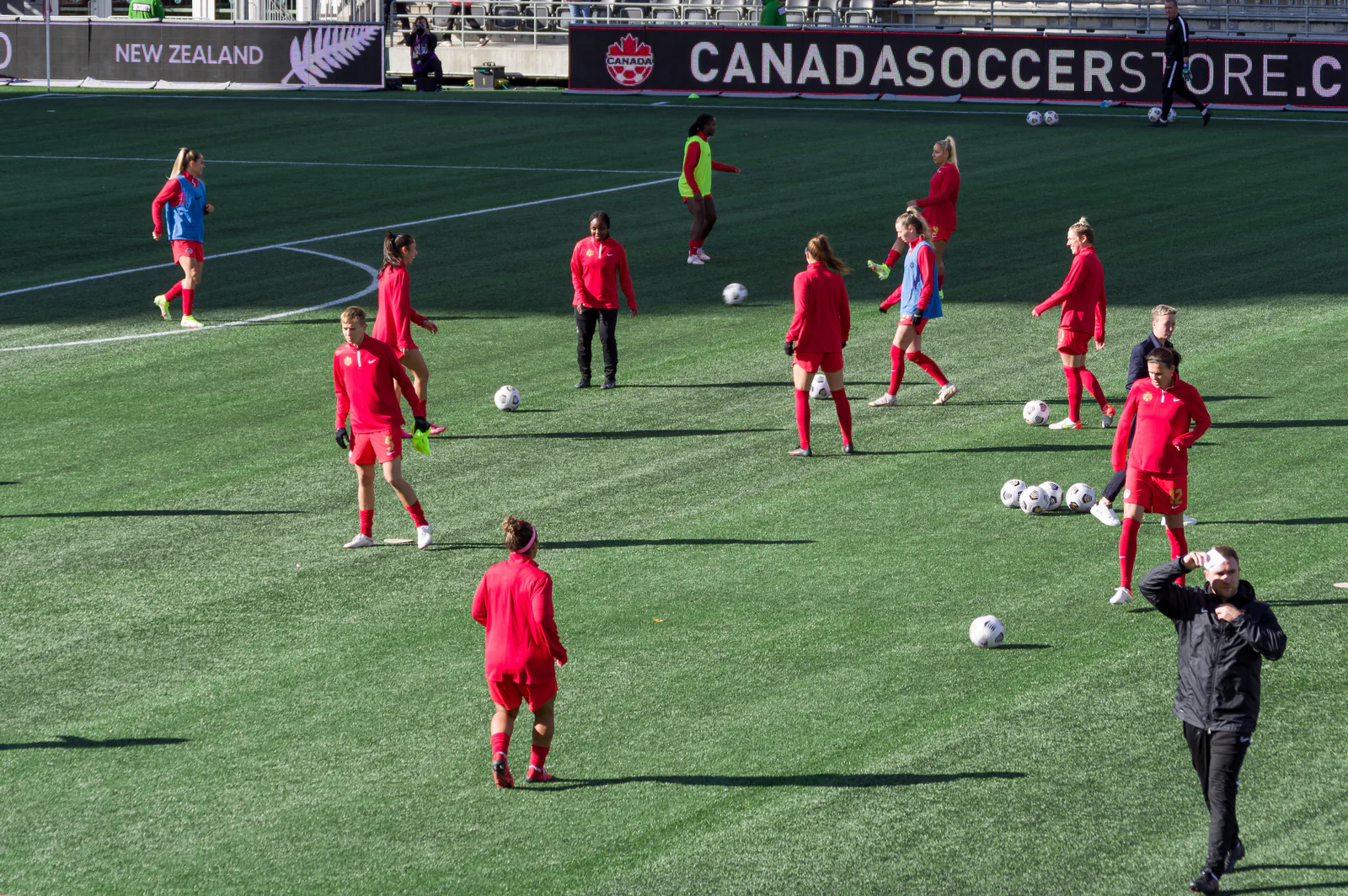 Canada women’s national-team players warming up on a field with balls and Canada Soccer signage.