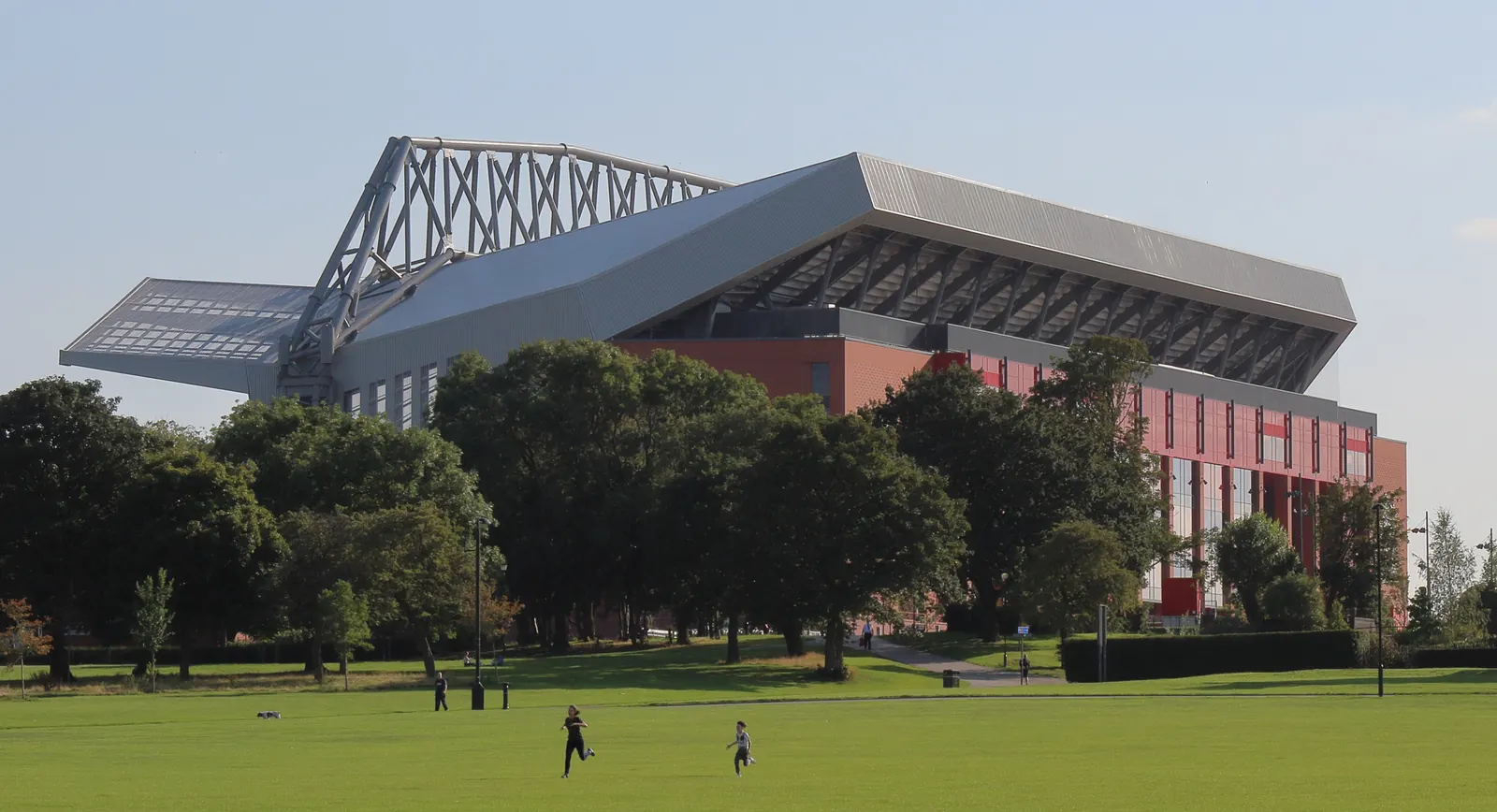 Anfield’s main stand beyond trees and people on the grass in Stanley Park.