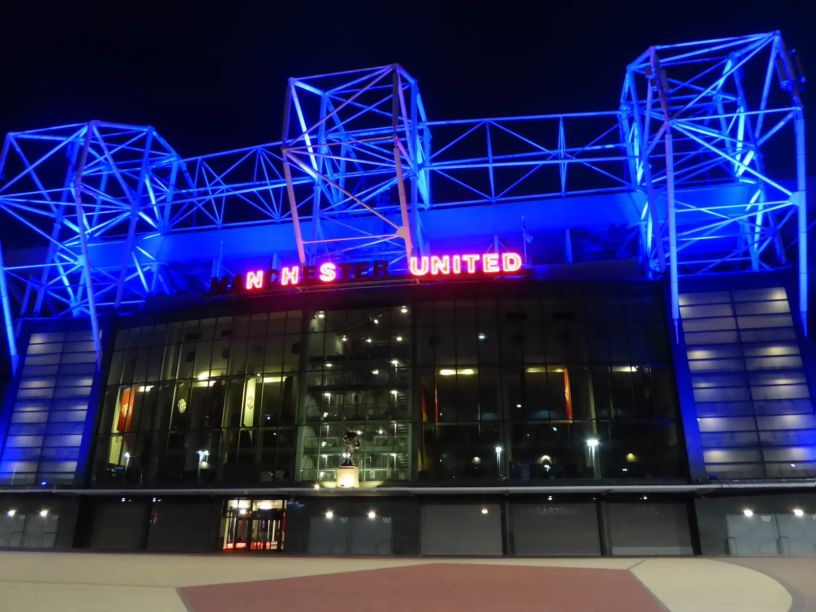 Old Trafford’s exterior illuminated blue at night.